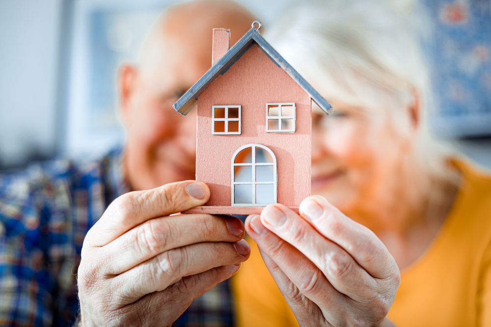 Senior couple holding up a small wooden home
